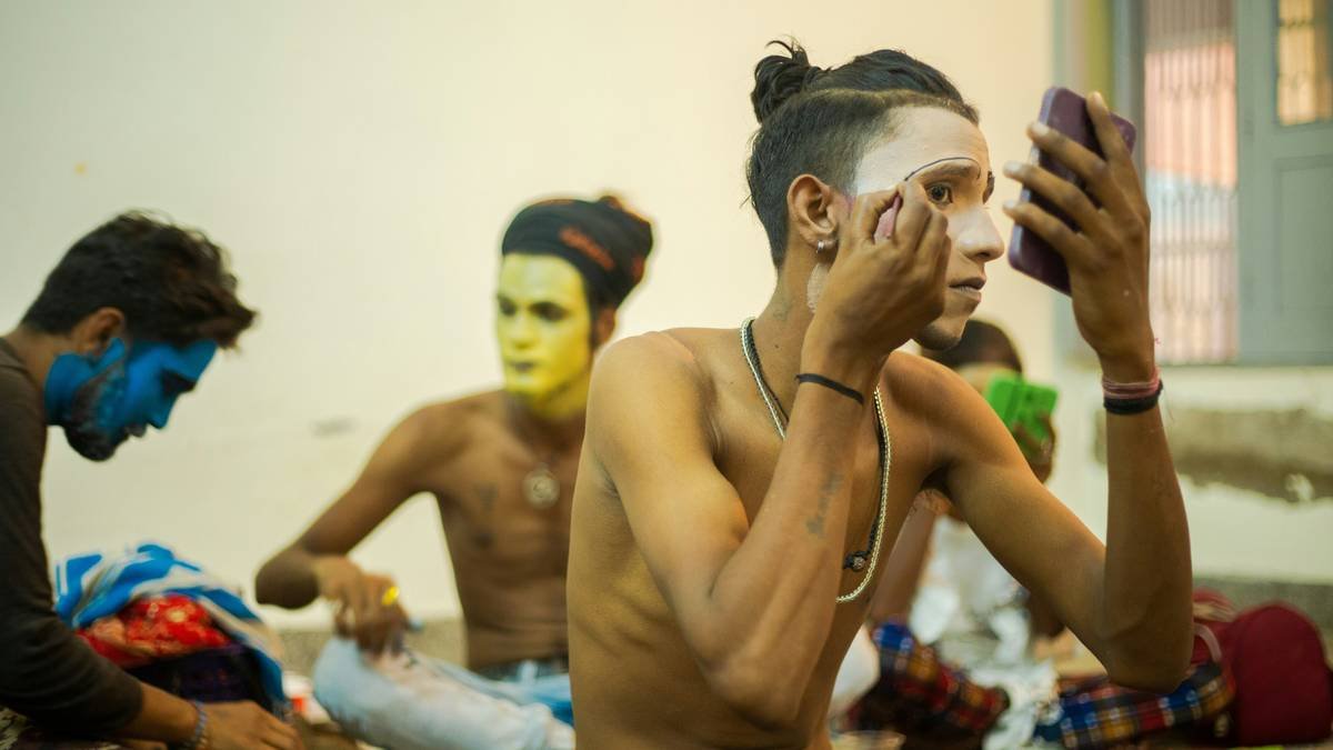 Close-up of hands gently applying special effects makeup remover to a face covered in dried latex and fake blood